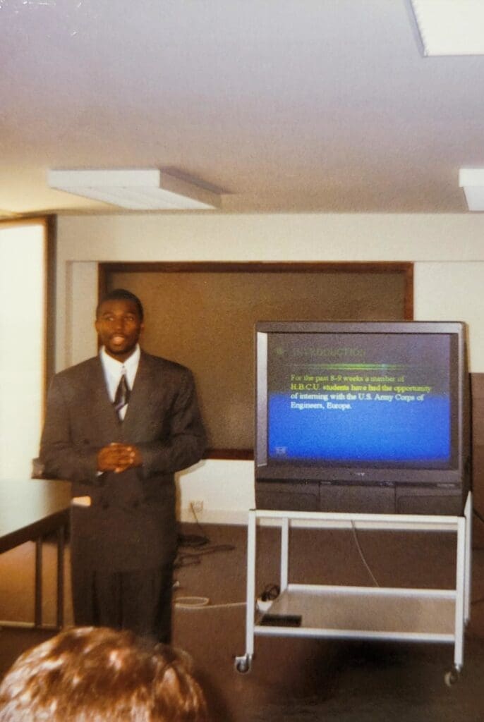 Man in suit presenting beside television monitor