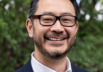 Smiling man in glasses and suit outdoors.